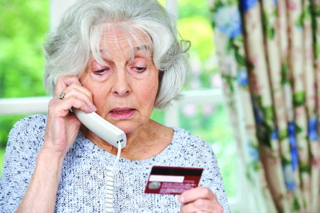 Stock photo of an elderly woman on the phone looking at her credit card.