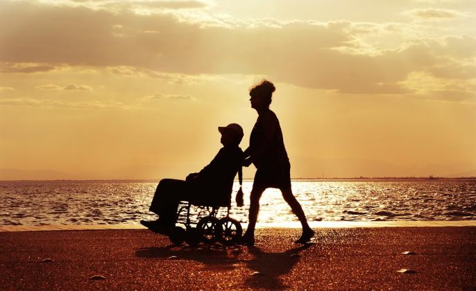 A photo of someone pushing someone else in a wheelchair on the beach.