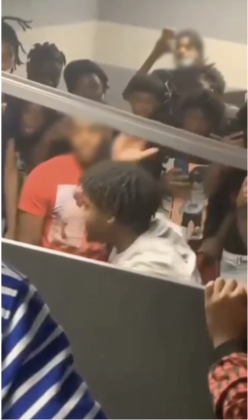 An apparent student-referee starts a boxing match while at least 20 teenage boys pack a bathroom to watch